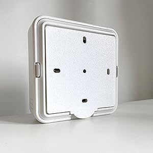 Appareil carré en plastique blanc avec de multiples petits trous et ouvertures sur sa face. Semblable à une unité électronique murale avec une