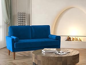 Modern bright blue velvet loveseat with wooden legs, positioned in a room with a vaulted fireplace and a round wooden coffee table