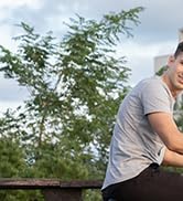 Vista parcial de una persona con una camiseta gris al aire libre cerca de un follaje verde, posiblemente realizando una actividad física.