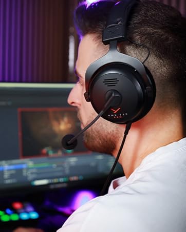 Casque de jeu supra-auriculaire avec microphone porté par l'utilisateur. Casque noir avec accents rouges visibles. Écran d'ordinateur orienté vers l'utilisateur avec affichage coloré.