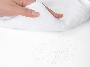 Weißer Stoff mit Wassertröpfchen auf der Oberfläche. Von Hand anhebbare Ecke, die die wasserabweisenden oder wasserdichten Eigenschaften des Materials demonstriert