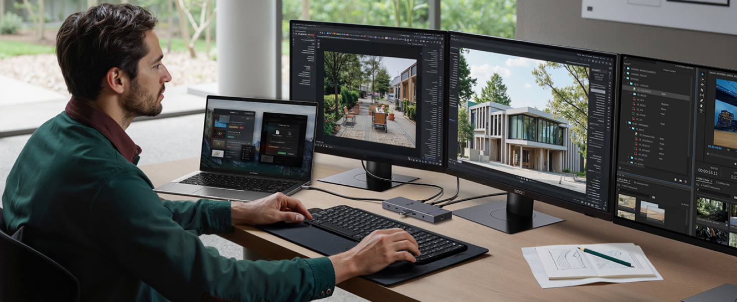 Man using multi-monitor setup for photo editing. Three large screens display different images and software interfaces. Laptop and keyboard visible on desk.