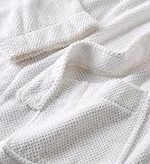 Close-up of white textured fabric, showing a soft, waffle-like pattern with folds and creases visible.