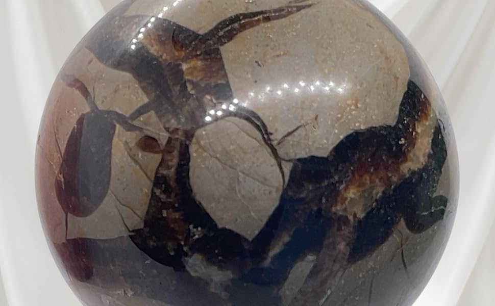 Große sphärische Kristall- oder Glaskugel mit dunklen Wirbelmustern, montiert auf einem durchsichtigen Acrylständer vor weißem Stoffhintergrund.