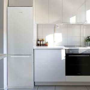 Cocina blanca moderna con refrigerador independiente, horno empotrado y elegantes gabinetes. La luz del sol entra por la ventana e ilumina el mostrador.
