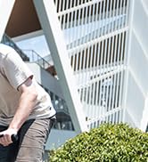 La mano de una persona extiende la mano a través de los listones blancos de la cerca para recortar el follaje verde. Muestra las actividades de jardinería o mantenimiento al aire libre a través de una barrera