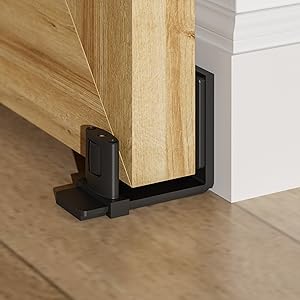 Nahaufnahme einer schwarzen L-förmigen Bodenführung für ein Scheunenschiebetor, das an der Basis einer Holztürverkleidung auf einem Hartholzboden angebracht