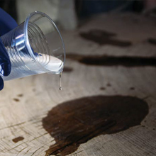 A gloved hand pours epoxy from a plastic cup onto a wood surface
