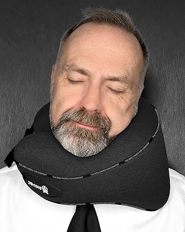 Black travel neck pillow with adjustable closure, shown providing head and neck support during rest.