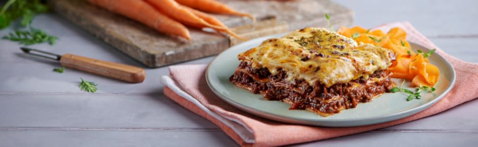 lasagne on table with carrots in the background