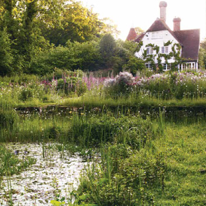 a house with a meadow and pond in front from beyond the garden