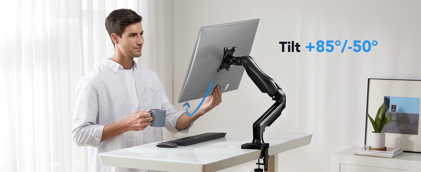 Adjustable monitor arm mounted to desk, demonstrating tilt range of +85°/-50° with screen attachment capability.