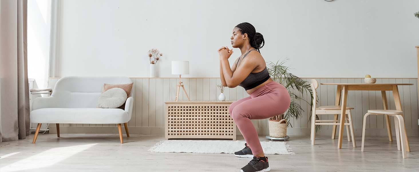 con leggings rosas y top negro realizando un ejercicio de sentadillas en un ambiente hogareño con