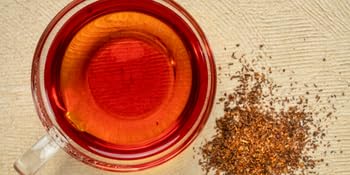 un tazón de té de vidrio con un líquido rojo y un montón de hojas de té secas.