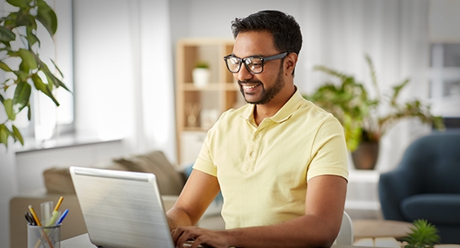 Personne assise à un bureau avec un ordinateur portable et un smartphone, montrée des épaules vers le bas dans une tenue décontractée travaillant à domicile.