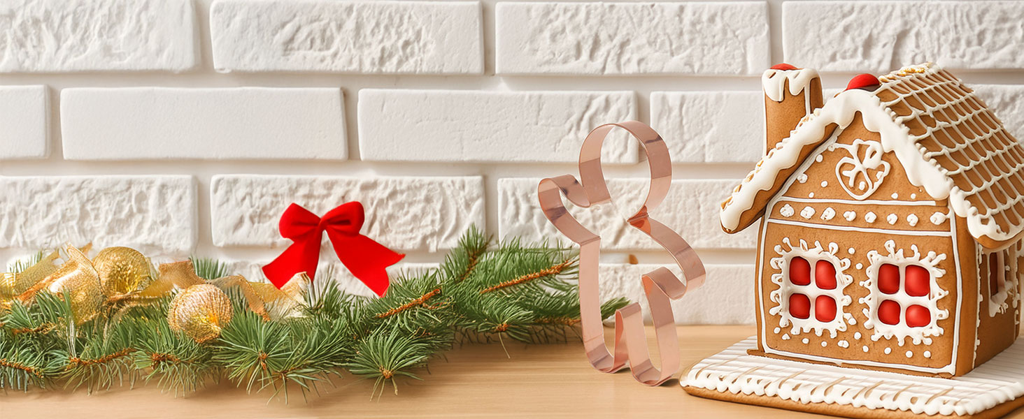 Copper gingerbread man cookie cutter displayed on a shelf next to a decorated gingerbread house.