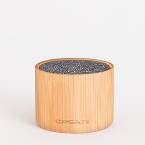 Recipiente cilíndrico de bambú con superficie superior de tela o fieltro gris oscuro. Diseño simple y minimalista sobre fondo blanco.