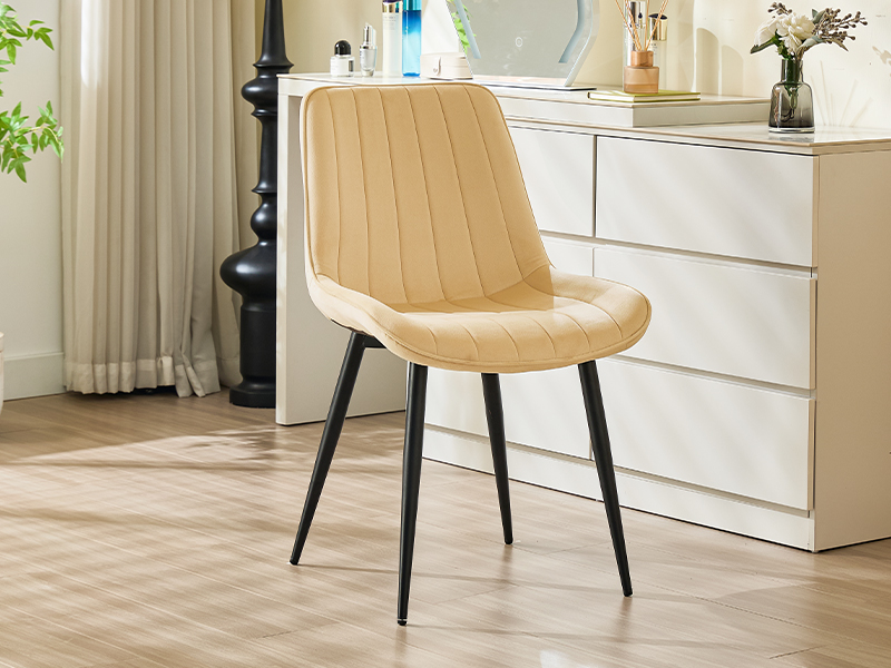 Beige upholstered dining chair with vertical channel stitching on the seat back. Black metal legs. Shown in a modern kitchen setting.