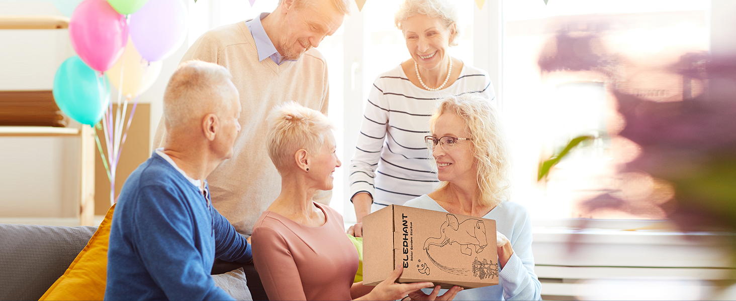 Group engaged in casual social activity around a table with colorful balloons visible in background, suggesting celebratory setting.