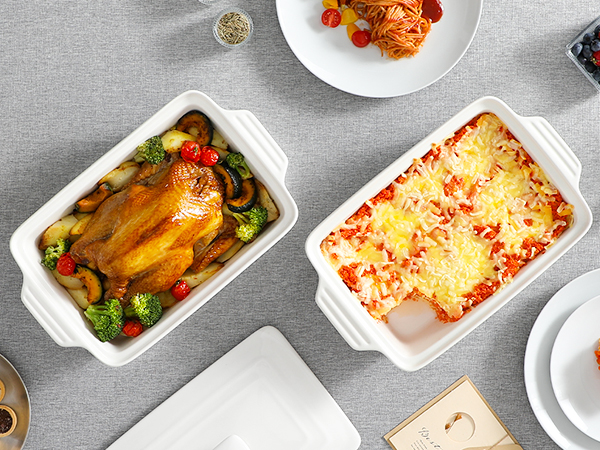 Two white ceramic baking dishes on grey surface - one containing a roasted whole chicken with vegetables, another with a cheese-topped casserole dish.