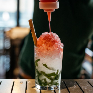 LYCHEE SWIZZLE as someone adds a red liquid to the white ice shavings with green leaves.