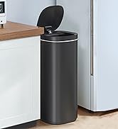 Tall cylindrical matte black touchless trash can with motion sensor lid, shown in a kitchen setting next to white cabinetry.