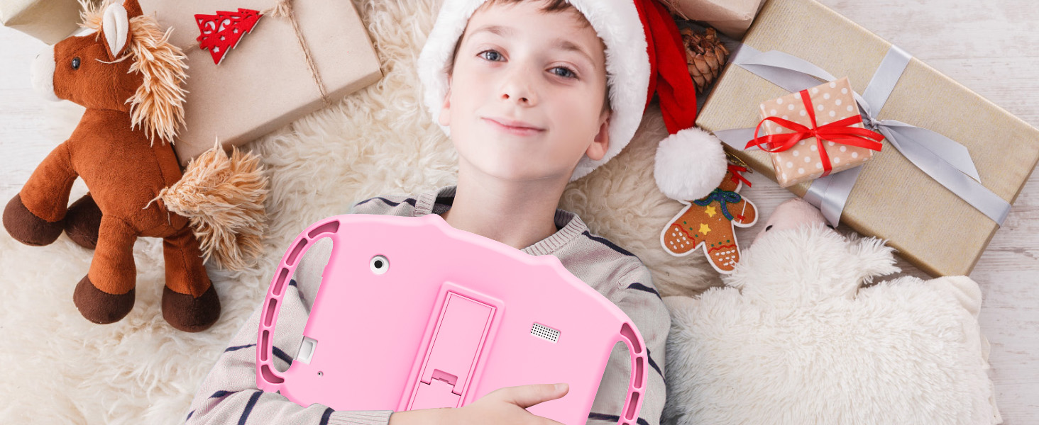 Pink children's camera surrounded by holiday items including wrapped gifts, plush reindeer, and gingerbread ornament on light carpet.
