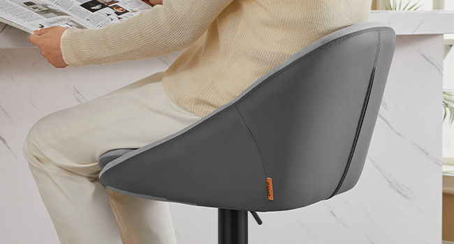 Gros plan d'un dossier de chaise de bureau gris foncé au design incurvé, mettant en valeur sa forme ergonomique et sa texture lisse. Une personne vêtue de vêtements beiges est assise.