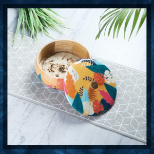 Tigela de madeira em uma superfície com padrão geométrico contendo um tecido colorido com padrão de folhas ou peça de vestuário.