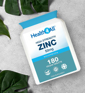 White bottle of zinc dietary supplement tablets on a white surface with green leaves. Label shows 180 tablets, likely indicating bottle contents.