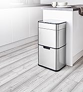 Modern stainless steel trash can with two-tier design featuring separate compartments, positioned against white kitchen wall and light wood flooring.