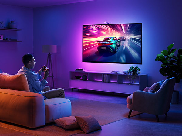 a man sitting in a chair in a living room playing a video game on a smart tv.