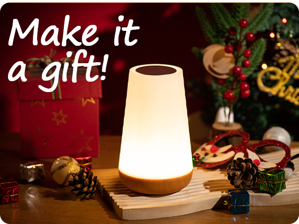 Modern table lamp with white conical shade and wooden base displayed in festive holiday setting with pine cones and decorations.