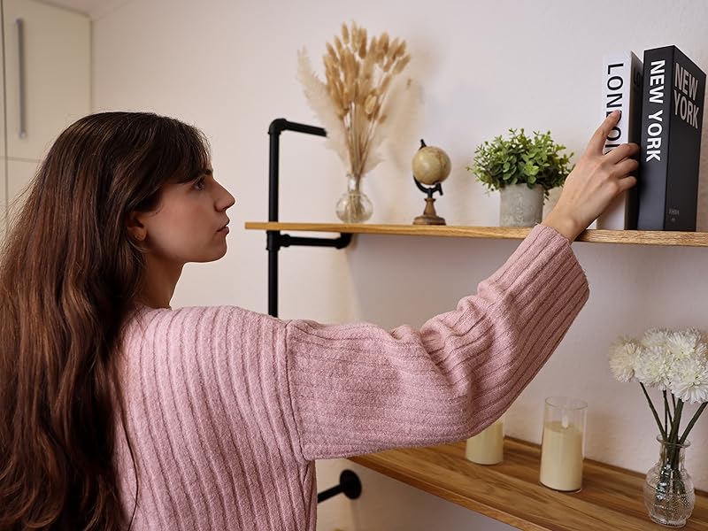Industrial-style wooden shelving with black metal brackets mounted on wall, displaying books, dried flowers, and decorative items.
