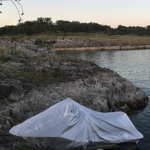 silver jet ski cover installed on ski in a lake with rocky outcropping and trees in background