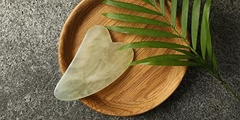 Gua Sha tool inside a wooden bowl with a palm frond resting next to it 