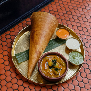 DOSA on a metal plate served with four other sauces with a redish orange tile background