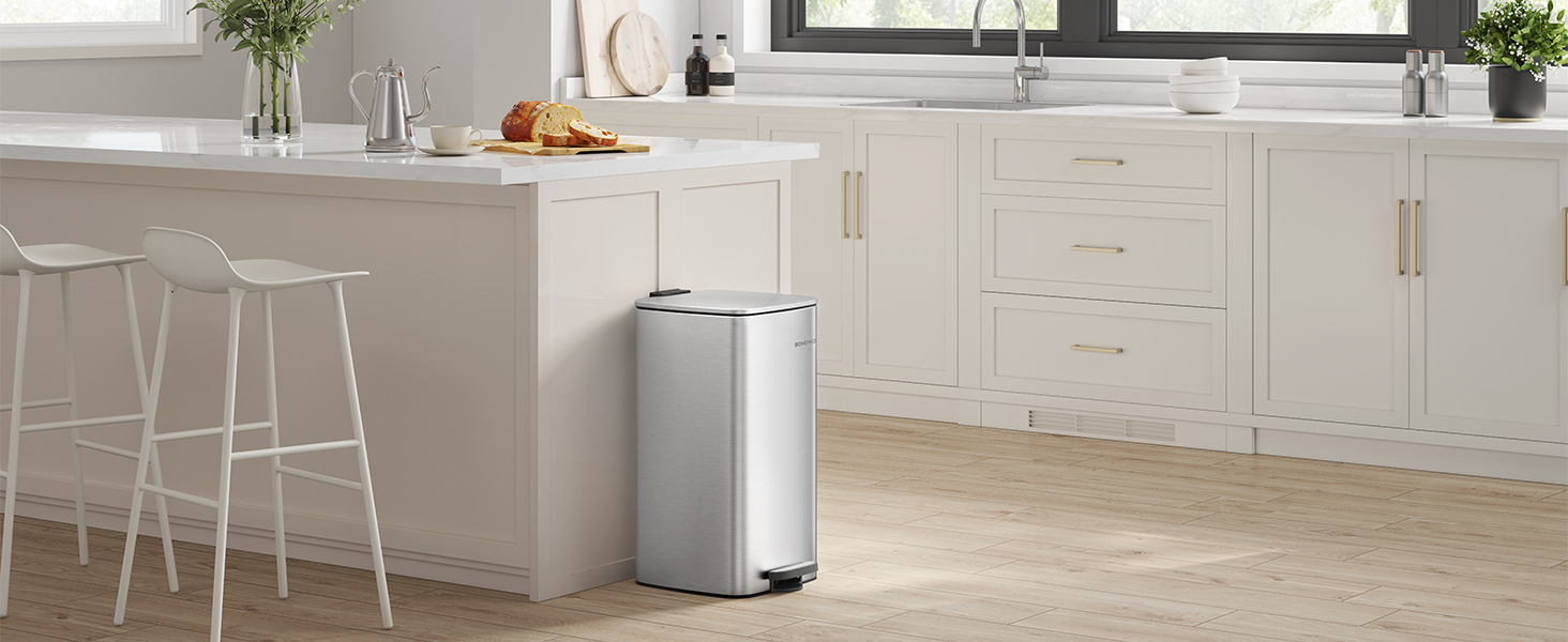 Modern stainless steel trash can positioned in a contemporary white kitchen with minimalist cabinetry and countertops.