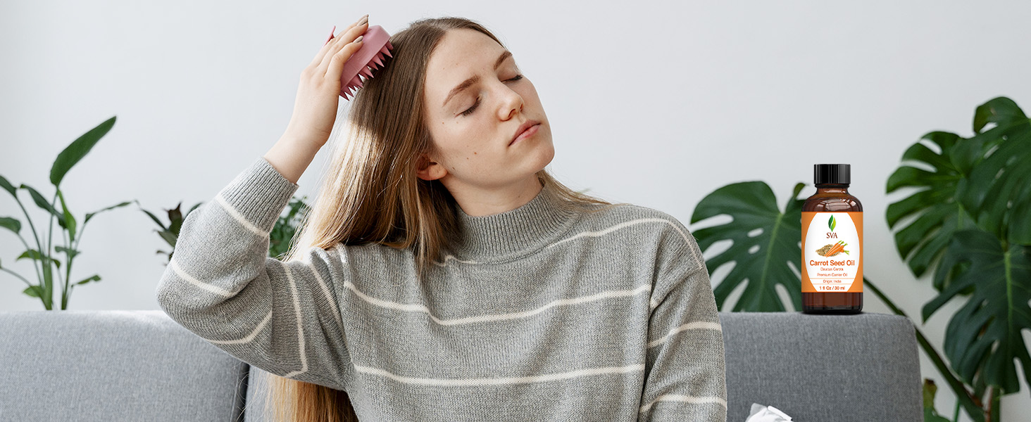 A lady massaging her hairs with comb using carrot seed carrier oil from amber bottle for haircare