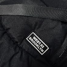Close-up of black fabric material with rectangular white logo patch stitched onto the surface.