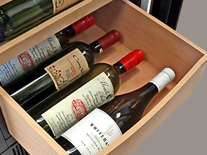 Closeup of beechwood drawer partly pulled out of the wine fridge with four bottles of wine showing