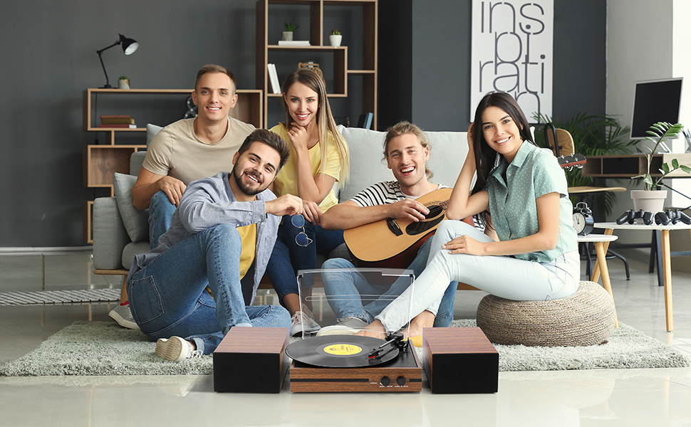 Vintage-style record player with wooden base and speakers, playing a vinyl record as people gather in a living room.
