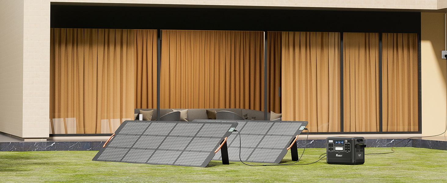 Outdoor solar panel array in a grassy area. Multiple panels are arranged in rows, tilted at an angle. A building with wood paneling is visible in the background.