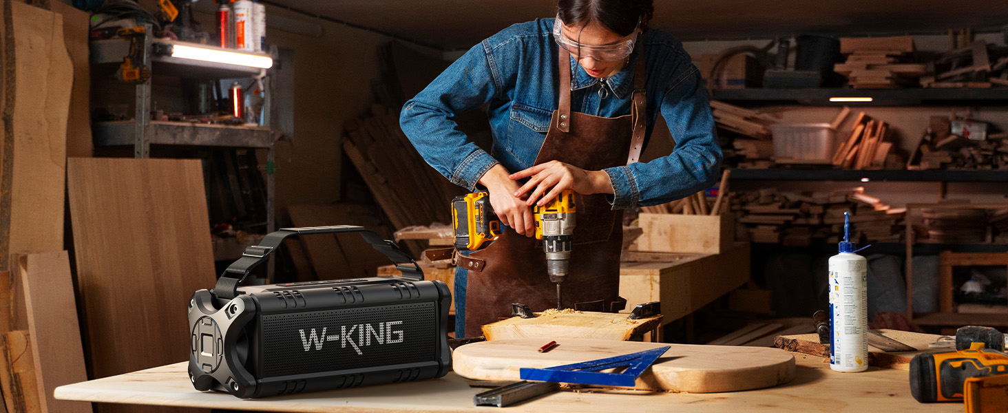 A cordless power drill in use on a wooden workbench, with a W-KING branded speaker visible in the foreground alongside woodworking tools.