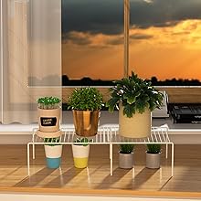 Window view of sunset over water. Indoor ledge with potted plants, glass of juice, and decorative items visible.