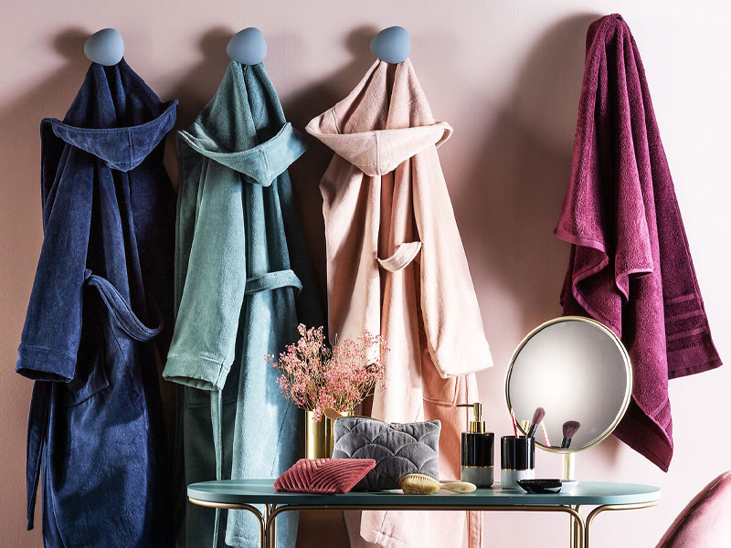 Scena da bagno con quattro asciugamani appesi in blu, verde, rosa e viola. Il tavolo da trucco espone oggetti decorativi e articoli da toeletta