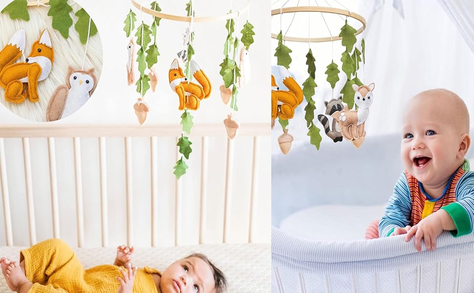 Babybett mit Hängemobil mit Waldtieren und Blättern. Zwei Säuglinge sind abgebildet, eines liegt im Kinderbett, ein anderes sitzt auf