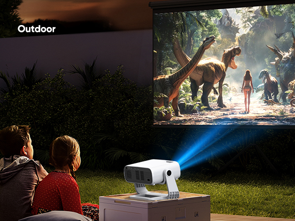 Portable outdoor projector displaying a dinosaur movie on a large screen. People sit on grass watching. Projector emits bright blue light in nighttime setting.