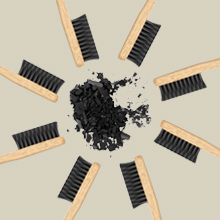 Disposición circular de cepillos de dientes con mango de madera y cerdas negras que rodean una pila de polvos o gránulos blancos y negros sobre