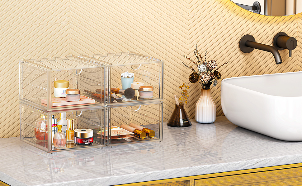 Clear acrylic organizer with multiple compartments on bathroom counter. Contains beauty products and toiletries. Near white sink, textured wall, and decorative vase with dried flowers.